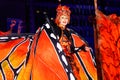 Woman on stilts in fancy orange butterfly costume